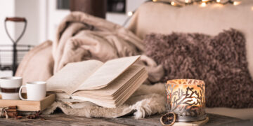 Cosy winter setting with cups, books, candles, and blankets for a warm and inviting home atmosphere