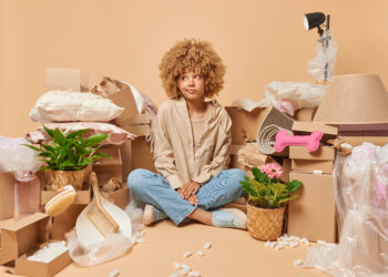 Thoughtful woman surrounded by boxes while decluttering her home, focusing on rubbish clearance and organisation