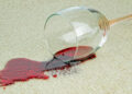 A glass of red wine spilled on a beige carpet, showcasing a common stain cleaned with eco-friendly solutions.