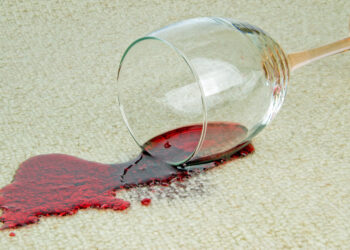 A glass of red wine spilled on a beige carpet, showcasing a common stain cleaned with eco-friendly solutions.