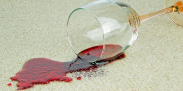 A glass of red wine spilled on a beige carpet, showcasing a common stain cleaned with eco-friendly solutions.