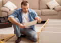 Man completing flat pack furniture assembly at home while reading instructions