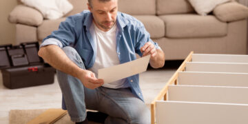 Man completing flat pack furniture assembly at home while reading instructions