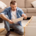 Man completing flat pack furniture assembly at home while reading instructions