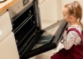 Young girl looking into an open oven before her school
