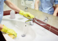 Person wearing gloves cleaning a bathroom sink with running water.