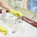 Person wearing gloves cleaning a bathroom sink with running water.