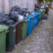 Overflowing outdoor bins and rubbish bags in a residential alley during summer.
