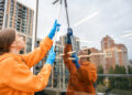 Woman cleaning tall window with squeegee on balcony.