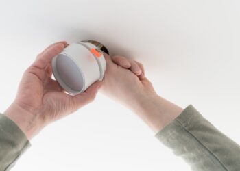 A homeowner inspecting a clean fireplace and chimney, with smoke alarms visible on the wall, preparing for a safe autumn or winter fire.