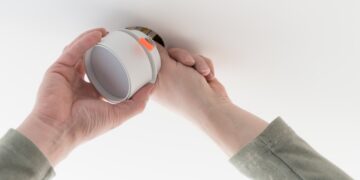 A homeowner inspecting a clean fireplace and chimney, with smoke alarms visible on the wall, preparing for a safe autumn or winter fire.