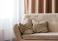A cosy UK living room with freshly cleaned curtains and a soft sofa, sunlight streaming through spotless windows before winter.