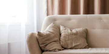 A cosy UK living room with freshly cleaned curtains and a soft sofa, sunlight streaming through spotless windows before winter.