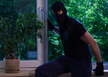 A suburban UK home at dusk with lights off, long shadows across the garden, and autumn leaves scattered around, symbolising how darker evenings increase burglary risks.