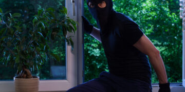 A suburban UK home at dusk with lights off, long shadows across the garden, and autumn leaves scattered around, symbolising how darker evenings increase burglary risks.