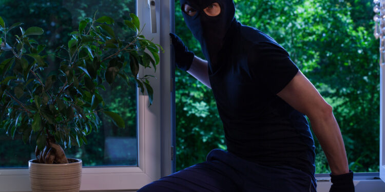 A suburban UK home at dusk with lights off, long shadows across the garden, and autumn leaves scattered around, symbolising how darker evenings increase burglary risks.