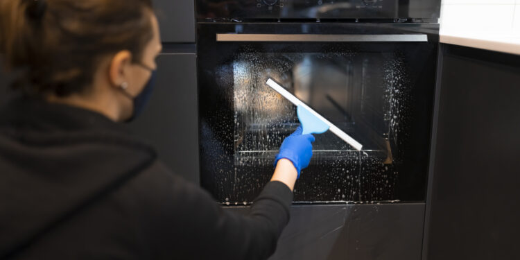 Clean oven in a modern UK kitchen with a packed suitcase nearby, highlighting the importance of oven cleaning before going on holiday.