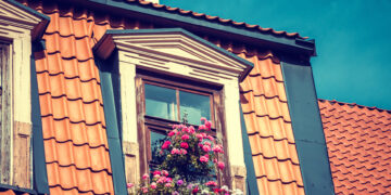 Professional window cleaner using safety equipment to clean upstairs windows on a residential property.