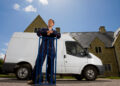 Man in work overalls leaning on a hand truck beside a white removal van outside a residential property in the UK