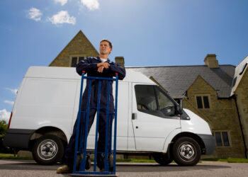 Man in work overalls leaning on a hand truck beside a white removal van outside a residential property in the UK