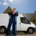 Man in work overalls leaning on a hand truck beside a white removal van outside a residential property in the UK
