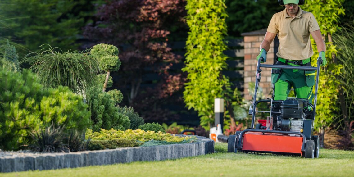 Person mowing a green lawn in a residential garden using a push lawnmower on a sunny day.