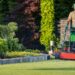 Person mowing a green lawn in a residential garden using a push lawnmower on a sunny day.