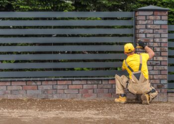 Worker installing horizontal metal fence panels beside a brick pillar in a garden boundary
