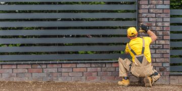 Worker installing horizontal metal fence panels beside a brick pillar in a garden boundary