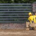 Worker installing horizontal metal fence panels beside a brick pillar in a garden boundary