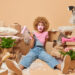 Woman surrounded by moving boxes and packing materials looking overwhelmed while holding a paint roller during house clearance preparation
