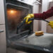 Professional oven cleaner using a steam tool to remove grease from the inside of a kitchen oven.