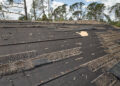 Wind-damaged house roof with missing and torn asphalt shingles exposing underlayment