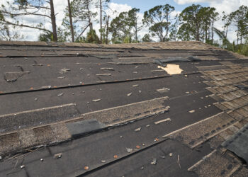 Wind-damaged house roof with missing and torn asphalt shingles exposing underlayment
