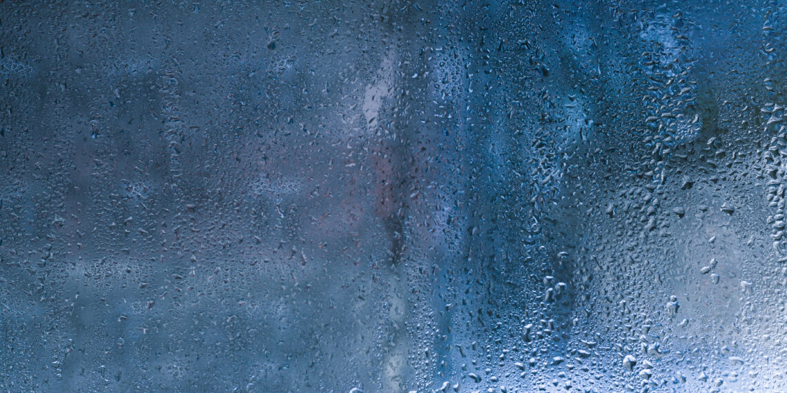 Condensation droplets forming on a cold window glass surface inside a home, showing moisture build-up