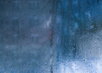 Condensation droplets forming on a cold window glass surface inside a home, showing moisture build-up