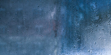 Condensation droplets forming on a cold window glass surface inside a home, showing moisture build-up