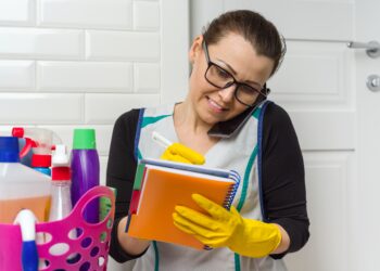 Homeowner in kitchen preparing to clean while reviewing household tasks before booking a professional service.