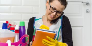 Homeowner in kitchen preparing to clean while reviewing household tasks before booking a professional service.