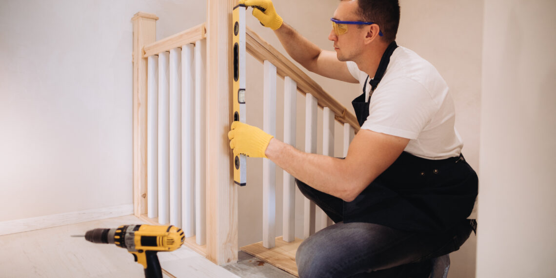 Close-up of a loose wooden stair banister being tightened with a screwdriver, showing slight movement at the wall fixing.