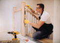 Close-up of a loose wooden stair banister being tightened with a screwdriver, showing slight movement at the wall fixing.