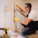 Close-up of a loose wooden stair banister being tightened with a screwdriver, showing slight movement at the wall fixing.