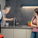 Emergency plumber inspecting leaking kitchen tap while concerned homeowner looks on in modern UK kitchen