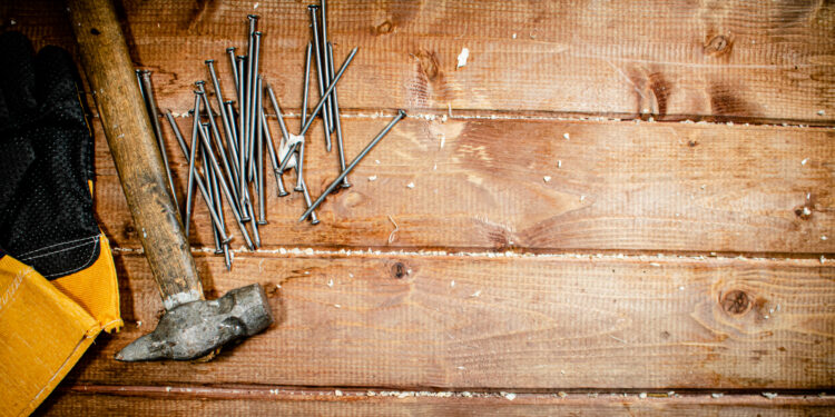 Close-up of a squeaky floorboard being fixed through carpet using a specialised repair screw tool, with the carpet intact.