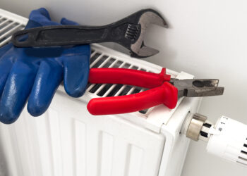 Tools and protective gloves placed on a household radiator with thermostatic valve, preparing for radiator bleeding or heating maintenance.