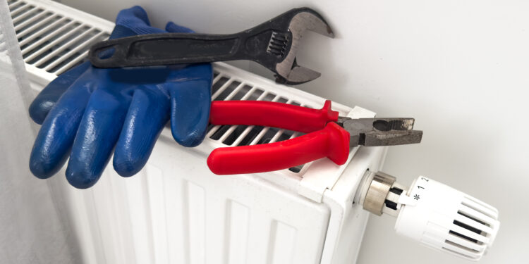 Tools and protective gloves placed on a household radiator with thermostatic valve, preparing for radiator bleeding or heating maintenance.