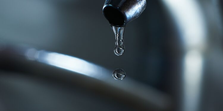 Plumber inspecting leaking kitchen tap while homeowner looks concerned about possible pipe issue in UK home