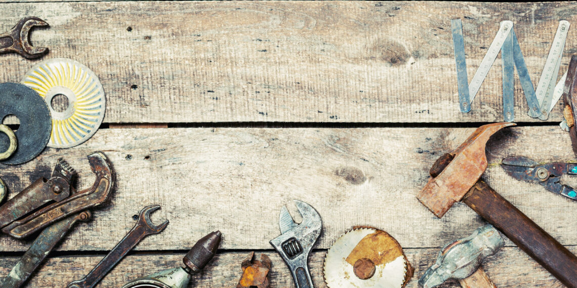 Assorted vintage hand tools including hammers, spanners and a folding ruler arranged on a rustic wooden workbench