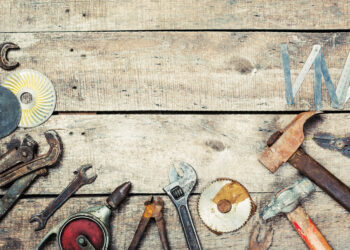 Assorted vintage hand tools including hammers, spanners and a folding ruler arranged on a rustic wooden workbench