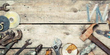 Assorted vintage hand tools including hammers, spanners and a folding ruler arranged on a rustic wooden workbench